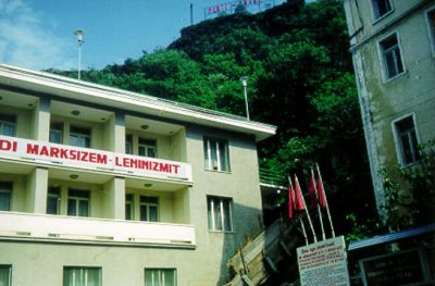 Gjirokastër – gatubild full av politisk propaganda: ”PARTI – ENVER” står det längst upp på höjden; på huset kan man läsa något om marxism-leninismen; under de röda fanorna kan man läsa om BPSH:s kongress (BPSH var något slags fackförening).